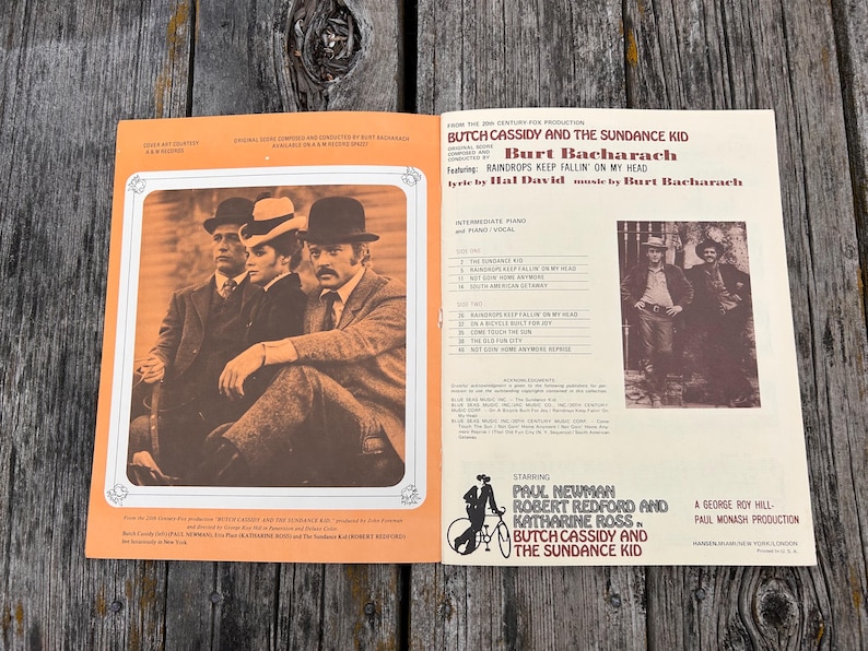 K&ouml;nnte beinhalten: Ein Vintage-Notenbuch f&uuml;r Klavier und Gesang zum Film Butch Cassidy und Sundance Kid. Das Cover zeigt ein sepiafarbenes Foto der Hauptfiguren, eine Titelliste sowie Credits f&uuml;r Burt Bacharach, Hal David, Paul Newman und Robert Redford.