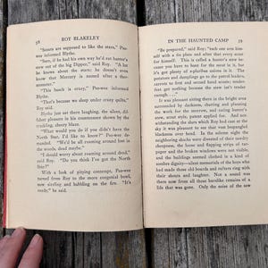 May include: An open vintage book titled Roy Blakeley In The Haunted Camp with pages 58 and 59 visible. The text is printed in black ink on off-white paper. The left page features dialogue between characters, while the right page continues the narrative.
