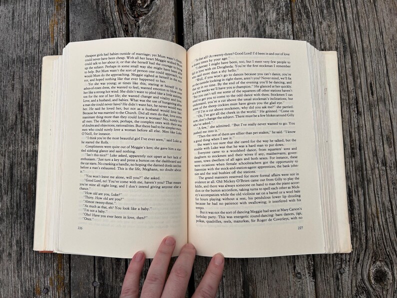 May include: An open hardcover book with cream-colored pages featuring black printed text. The left page is numbered 226 and the right page is numbered 227. The book is held open, displaying two full columns of narrative text in a serif font.