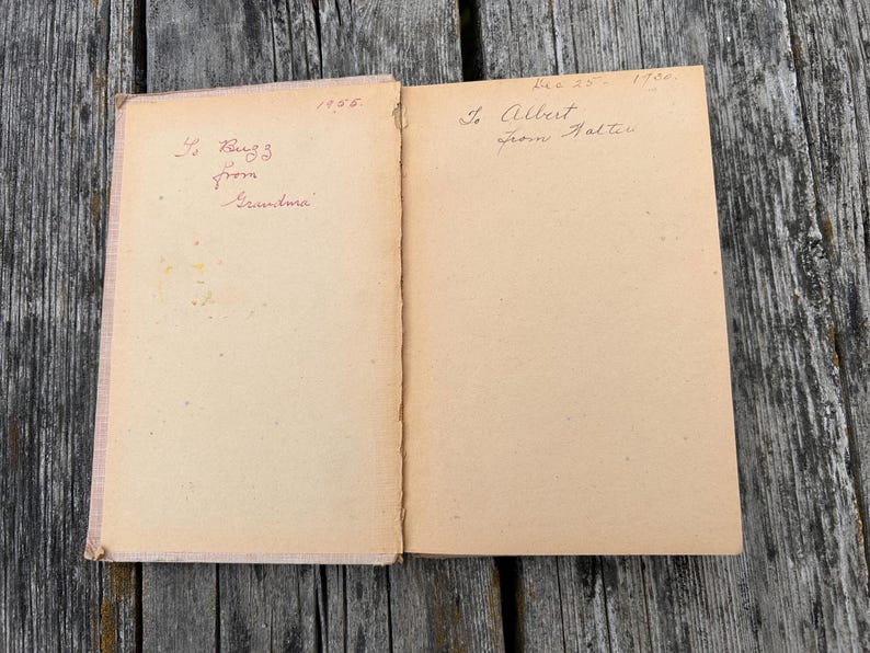 K&ouml;nnte beinhalten: Ein aufgeschlagenes altes Buch mit gealterten, hellbraunen Seiten. Die linke Seite zeigt handgeschriebenen Text in roter Tinte mit 'To Buzz from Grandma' und '1956'. Die rechte Seite enth&auml;lt handgeschriebenen Text in schwarzer Tinte mit 'Dec 25 - 1950' und 'To Albert from Walter'.