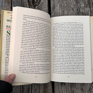 May include: An open hardcover book with cream-colored pages displaying printed black text. The left page shows page number 58 and the right page shows page number 59. The book features a partial dust jacket with green and black text on the spine.