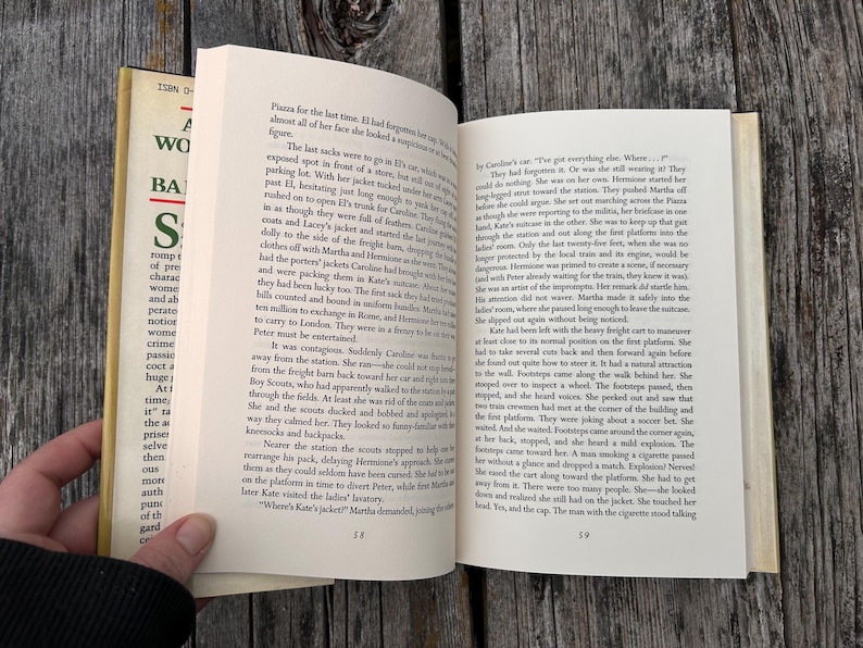 May include: An open hardcover book with cream-colored pages displaying printed black text. The left page shows page number 58 and the right page shows page number 59. The book features a partial dust jacket with green and black text on the spine.