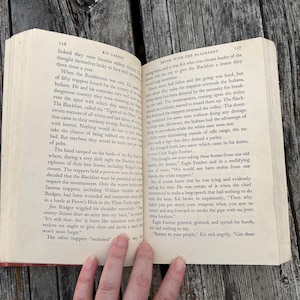May include: An open hardcover book with cream-colored pages featuring black printed text. The left page is numbered 116 and the right page is numbered 117, with the chapter title Brush with the Blackfeet visible at the top.