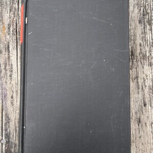 Pu&ograve; includere: Un libro con copertina rigida rettangolare rivestito in tessuto nero. Il dorso del libro presenta una piccola striscia decorativa rossa verticale vicino al bordo superiore. La superficie della copertina mostra lievi segni di usura.