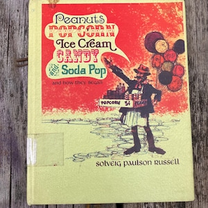 Puede incluir: Portada de libro vintage con diseño rojo y amarillo. Destacan las palabras "Peanuts, Popcorn, Ice Cream, Candy, Soda Pop", junto a una ilustración de un hombre vendiendo palomitas y globos. El libro se titula "and how they began".