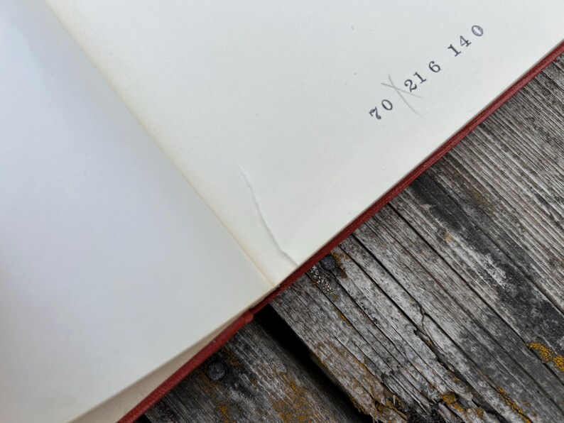 May include: An open book with cream-colored pages featuring a red cover edge. The top right corner of the page displays the printed numbers 70, 21, 6, and 140, with a faint diagonal line crossing through the number 21 in black ink.