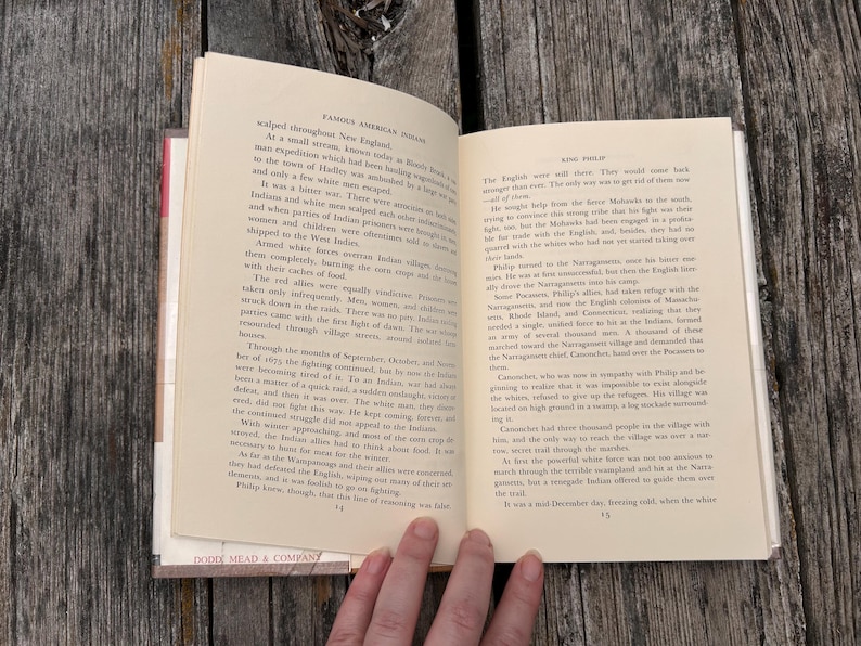 Puede incluir: Un libro de tapa dura abierto con p&aacute;ginas de color crema y texto impreso en negro. La p&aacute;gina izquierda est&aacute; numerada con el 14 y la derecha con el 15. El texto incluye los encabezados Famous American Indians y King Philip.