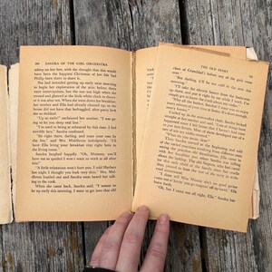 May include: An open vintage book with aged, cream-coloured paper pages featuring black printed text. The left page is titled Sandra of the Girl Orchestra and the right page is titled The Old Diary. The book shows signs of wear with visible binding.