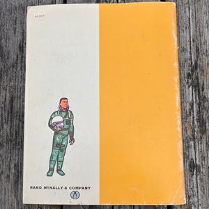 May include: A rectangular book cover featuring a vertical split design with a white left side and an orange right side. The white section displays a cartoon astronaut in a green suit holding a helmet, the text 93-2317, and Rand McNally & Company.