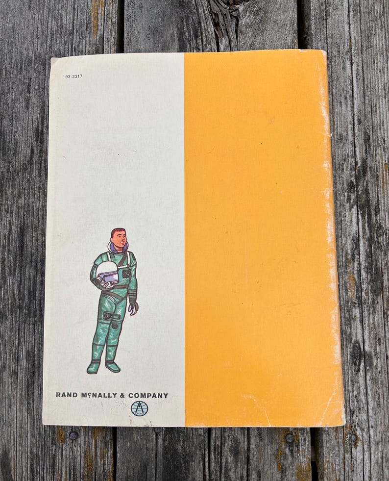 May include: A rectangular book cover featuring a vertical split design with a white left side and an orange right side. The white section displays a cartoon astronaut in a green suit holding a helmet, the text 93-2317, and Rand McNally & Company.