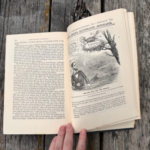 May include: An open book with cream-colored pages featuring black text and a historical political cartoon titled The Bad Bird and the Mudsill. The illustration depicts a man looking up at a bird in a nest labeled Richmond, from Frank Leslie's Illustrated Newspaper.