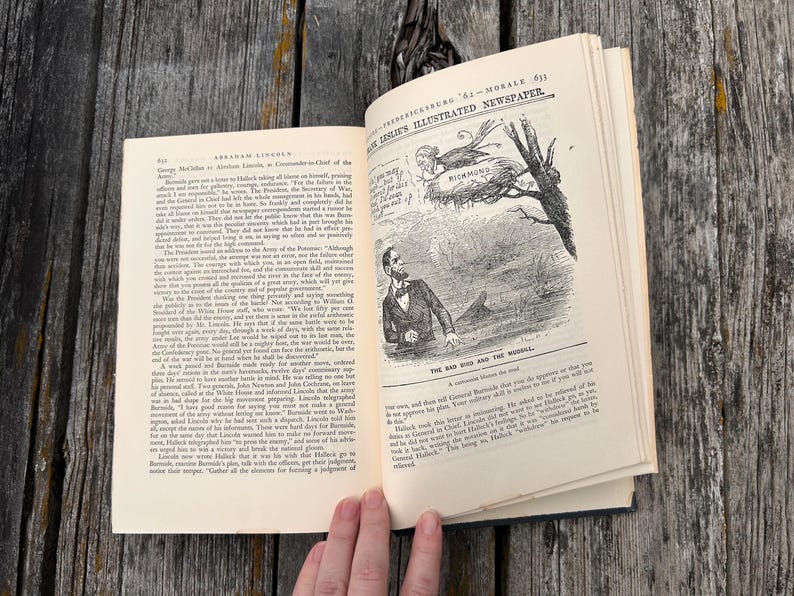 May include: An open book with cream-colored pages featuring black text and a historical political cartoon titled The Bad Bird and the Mudsill. The illustration depicts a man looking up at a bird in a nest labeled Richmond, from Frank Leslie's Illustrated Newspaper.