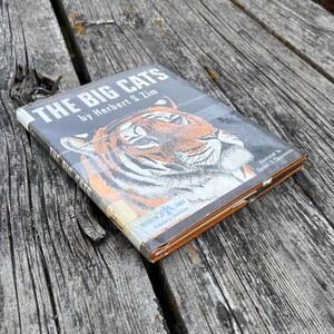 Puede incluir: Un libro de tapa dura titulado The Big Cats de Herbert S. Zim, con una ilustraci&oacute;n detallada de un tigre en la portada. El libro tiene una cubierta protectora de pl&aacute;stico de biblioteca e incluye el texto Library Edition y un logo de &aacute;guila.