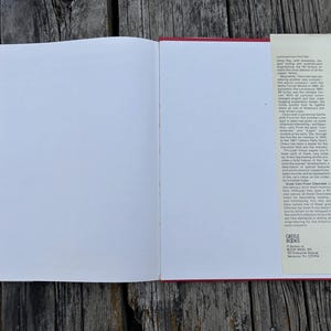 Op de afbeelding: Een open hardcover boek met lege witte pagina's en een beige stofomslagflap aan de rechterkant. De flap bevat gedrukte tekst over Chevrolet-auto's en de uitgever Castle Books, een divisie van Book Sales, Inc., Secaucus, NJ 07094.