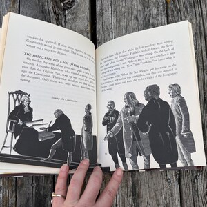 Puede incluir: Un libro abierto con ilustraciones en blanco y negro que representan a figuras hist&oacute;ricas firmando la Constituci&oacute;n. El texto describe a los delegados despidi&eacute;ndose y las observaciones de Benjamin Franklin sobre la silla.