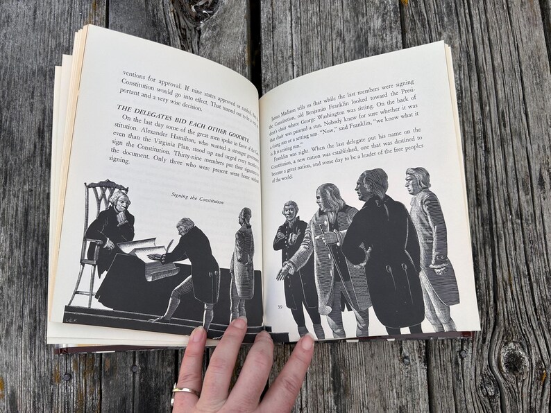 Puede incluir: Un libro abierto con ilustraciones en blanco y negro que representan a figuras hist&oacute;ricas firmando la Constituci&oacute;n. El texto describe a los delegados despidi&eacute;ndose y las observaciones de Benjamin Franklin sobre la silla.