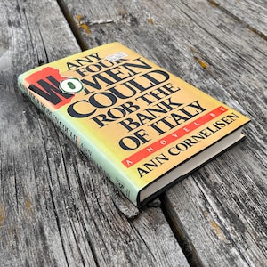 May include: A hardcover book titled Any Four Women Could Rob the Bank of Italy by Ann Cornelisen. The cover features a yellow to white gradient background with bold black text, a red accent bar, and a small green circular graphic on the front.