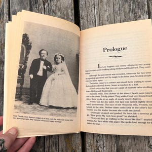 Pu&ograve; includere: Un libro aperto con pagine color crema. La pagina sinistra presenta una fotografia in bianco e nero di una persona in smoking accanto a una persona in abito da sposa. La pagina destra contiene testo sotto il titolo Prologue.