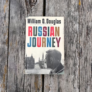 May include: A hardback book titled Russian Journey by William O. Douglas. The cover features a black and white photograph of a man in profile overlooking a city square with tall buildings, and the title text in red, blue, and brown.