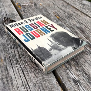 May include: A hardback book titled Russian Journey by William O. Douglas with a dust jacket featuring a black and white photograph of a cityscape and a person's profile. The title is printed in bold red and blue capital letters on a white background.