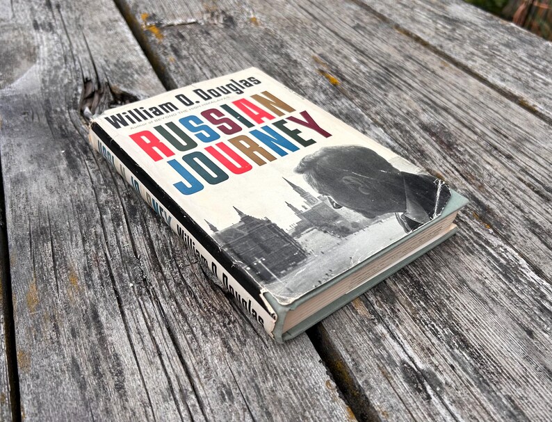 May include: A hardback book titled Russian Journey by William O. Douglas with a dust jacket featuring a black and white photograph of a cityscape and a person's profile. The title is printed in bold red and blue capital letters on a white background.
