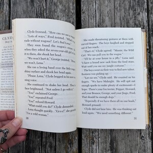 May include: An open book with white pages and black printed text, showing pages 30 and 31. The left page begins with dialogue from Clyde and Fred, while the right page continues the narrative about a girl named Lena and a group of boys.