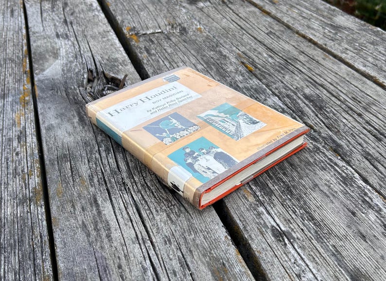 May include: A hardcover book titled Harry Houdini: Boy Magician by Kathryn Kilby Borland and Helen Ross Speicher. The cover features a tan background with three illustrations, including a person on a tightrope and a portrait of a young person.