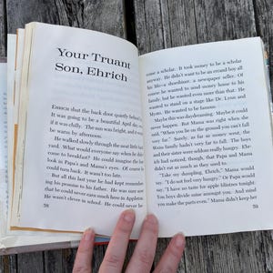 May include: An open book displaying pages 58 and 59, featuring the chapter title Your Truant Son, Ehrich. The text is printed in black ink on white paper, with page numbers at the bottom corners. The book is held open, revealing paragraphs of narrative text.