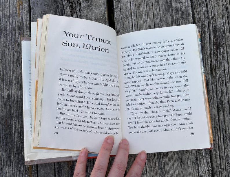 May include: An open book displaying pages 58 and 59, featuring the chapter title Your Truant Son, Ehrich. The text is printed in black ink on white paper, with page numbers at the bottom corners. The book is held open, revealing paragraphs of narrative text.