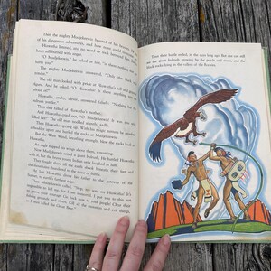 K&ouml;nnte beinhalten: Ein aufgeschlagenes altes Buch mit gedrucktem Text auf der linken Seite und einer farbigen Illustration auf der rechten Seite. Das Bild zeigt zwei Figuren in traditioneller Kleidung, einen gro&szlig;en braunen Adler und rote Felsen vor blauem Himmel.