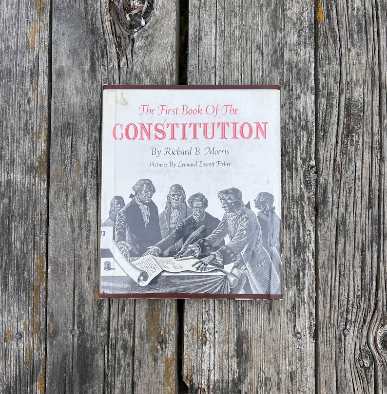 Puede incluir: Un libro de tapa dura titulado The First Book of The Constitution de Richard B. Morris con ilustraciones de Leonard Everett Fisher. La cubierta blanca presenta una ilustraci&oacute;n en blanco y negro de figuras hist&oacute;ricas firmando un documento.