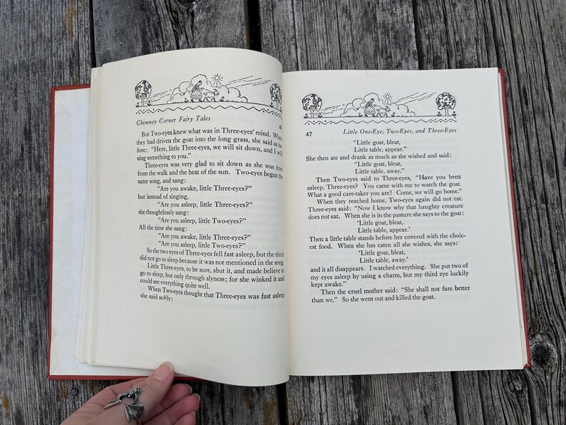 May include: An open hardcover book with cream-colored pages featuring black printed text and illustrations. The left page is titled Chimney Corner Fairy Tales, and the right page is titled Little One-Eye, Two-Eyes, and Three-Eyes with story text.