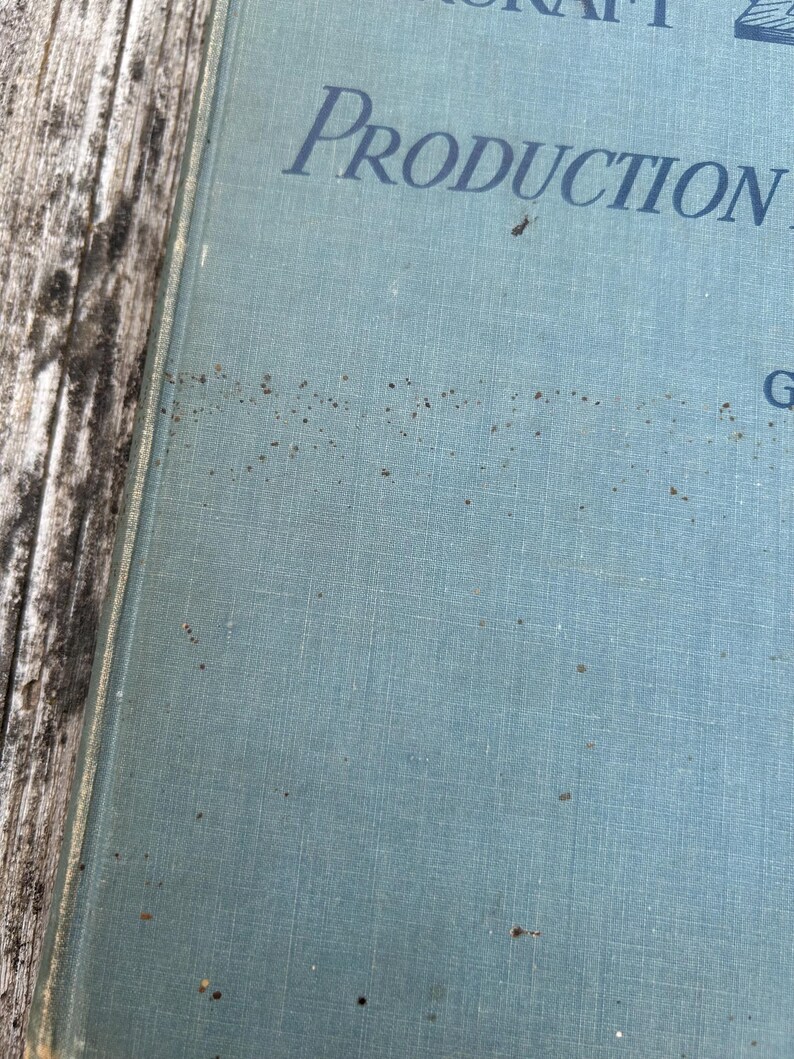 Pu&ograve; includere: Una copertina rigida di colore azzurro e testurizzata con testo in blu scuro che recita "PRODUCTION" e "G". La superficie della copertina mostra segni visibili di invecchiamento, tra cui macchie marrone scuro sparse e una consistenza simile al tessuto.