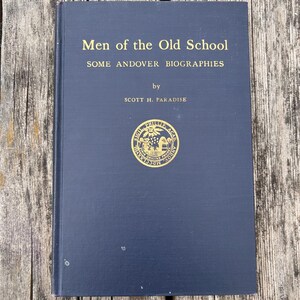 Może przedstawiać: Ciemnoniebieska książka w twardej oprawie zatytułowana Men of the Old School: SOME ANDOVER BIOGRAPHIES autorstwa Scotta H. Paradise'a. Okładka zawiera złote napisy oraz okrągły złoty emblemat pośrodku przedstawiający pieczęć z łacińskim tekstem.