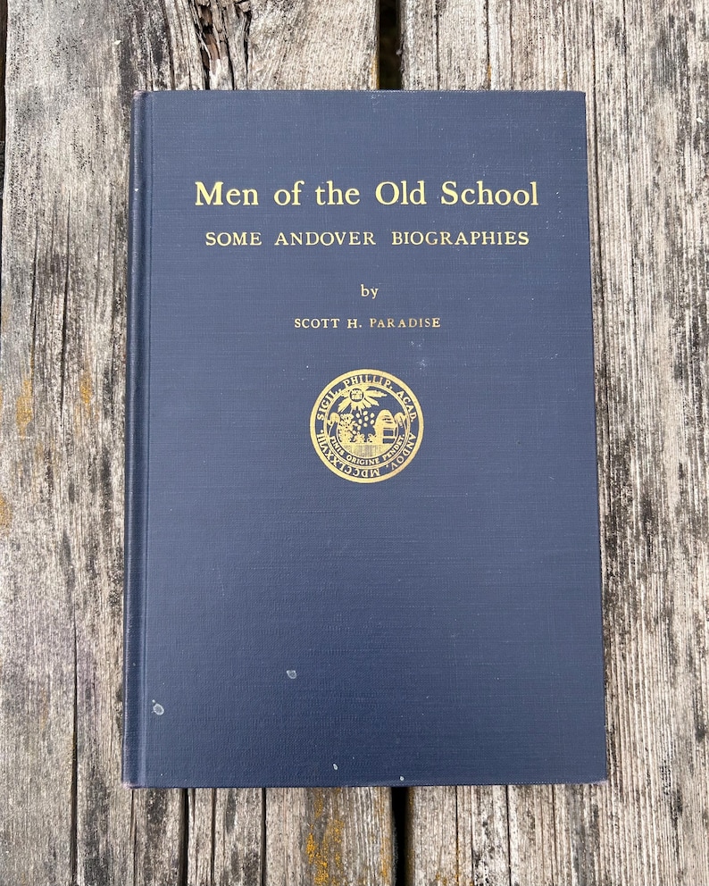 Może przedstawiać: Ciemnoniebieska książka w twardej oprawie zatytułowana Men of the Old School: SOME ANDOVER BIOGRAPHIES autorstwa Scotta H. Paradise'a. Okładka zawiera złote napisy oraz okrągły złoty emblemat pośrodku przedstawiający pieczęć z łacińskim tekstem.