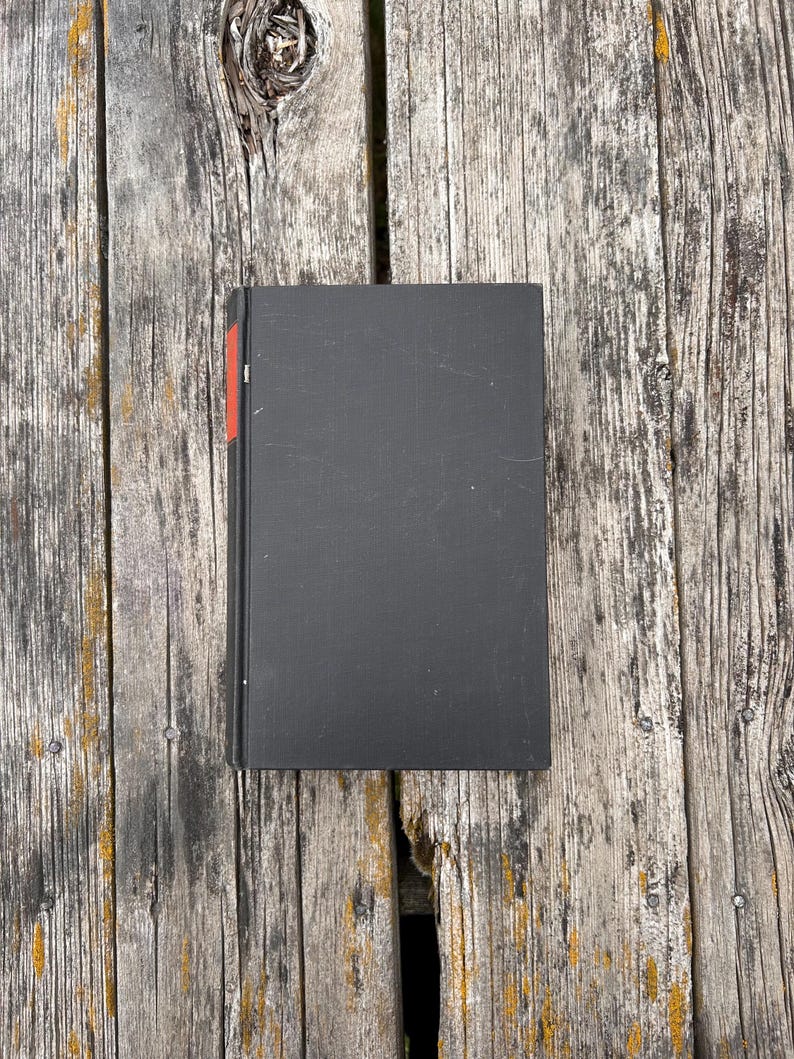 Pu&ograve; includere: Un libro rettangolare con copertina rigida nera e una sottile striscia verticale rossa lungo il bordo sinistro del dorso. Il libro &egrave; posizionato verticalmente e presenta una copertina pulita e semplice, priva di testo o grafiche visibili.