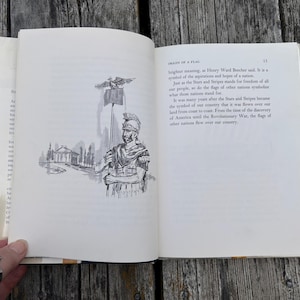May include: An open book with white pages featuring black ink text and a line drawing of a Roman soldier holding a flag pole with an eagle topper. The text on the right page is titled Origin of a Flag and discusses national symbols.