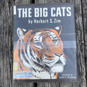 Puede incluir: Un libro de tapa dura titulado The Big Cats de Herbert S. Zim, ilustrado por Gardell D. Christensen. La cubierta negra presenta una ilustraci&oacute;n detallada de un tigre en naranja, negro y blanco, con una etiqueta de Morrow Eagle Library Edition abajo.