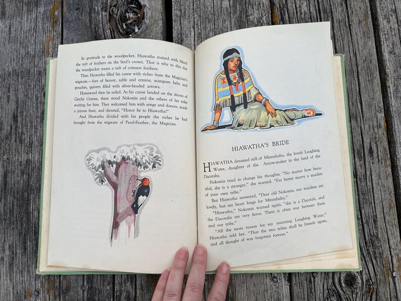 K&ouml;nnte beinhalten: Ein aufgeschlagenes altes Buch mit cremefarbenen Seiten, schwarzem Drucktext und zwei farbigen Illustrationen. Eine Abbildung zeigt eine Person in traditioneller Kleidung, die andere einen Specht auf einem Baumstamm. Das Buch hat einen gr&uuml;nen Buchr&uuml;cken.