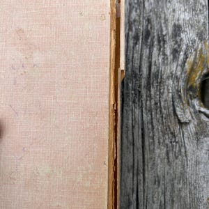 K&ouml;nnte beinhalten: Ein hellbeiges, texturiertes Hardcover-Buch mit sichtbaren Abnutzungserscheinungen an der Buchr&uuml;cken-Kante. Das Einbandmaterial weist Ausfransungen, kleine dunkle Flecken und leichte Verf&auml;rbungen auf, die auf Alter und Gebrauch hindeuten.