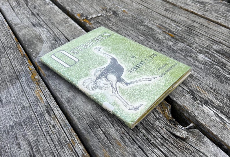 May include: A hardback book titled Ostriches by Herbert S. Zim with an illustration of an ostrich on the front cover. The cover features a textured light green background with white lettering and a black and white drawing of an ostrich.