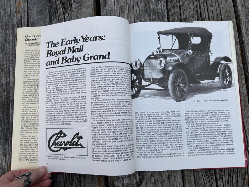 Op de afbeelding: Een open boekpagina met een zwart-witfoto van een 1914 Series H Royal Mail roadster. De tekst bevat de titel The Early Years: Royal Mail and Baby Grand, een Chevrolet-logo en kolommen met historische informatie over auto's.