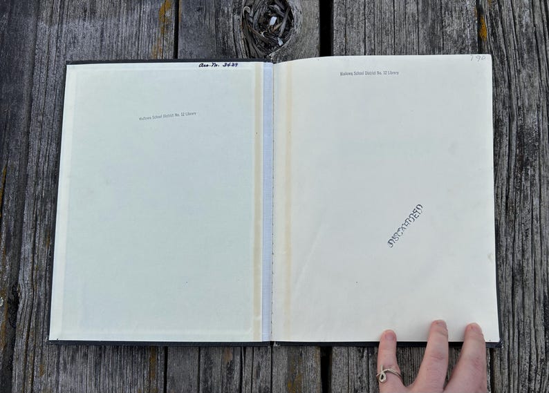 May include: An open book with cream-coloured pages featuring the text "Rahway School District No. 12 Library" printed at the top of both pages. The left page includes the handwritten text "Acc. No. 3639" and the right page has a black ink stamp.