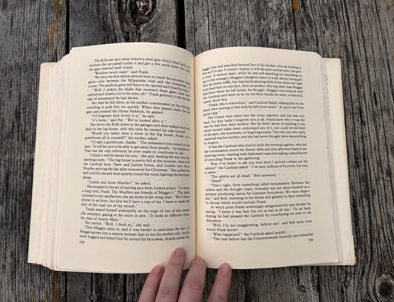 May include: An open paperback book with cream-colored pages featuring black printed text. The left page shows page number 598 and the right page shows page number 599. The book is held open, displaying two columns of narrative text in English.