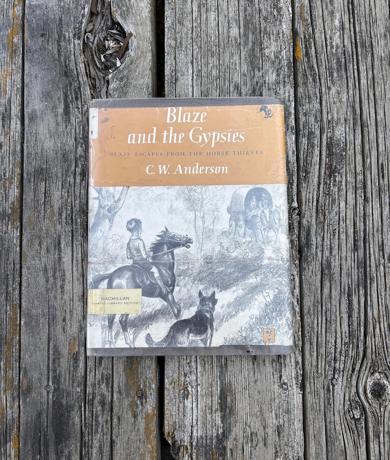 May include: A hardcover book titled Blaze and the Gypsies by C. W. Anderson, featuring a tan upper cover with black text and a black-and-white illustration of a child on a horse with a dog and a wagon below, plus a Macmillan library edition label.