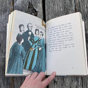 Puede incluir: Un libro de tapa dura abierto que muestra una p&aacute;gina con una ilustraci&oacute;n en blanco y negro de cuatro personas con ropa de &eacute;poca y una p&aacute;gina de texto impreso. El texto incluye las palabras: "Not in vain do we watch the setting and rising of the stars."