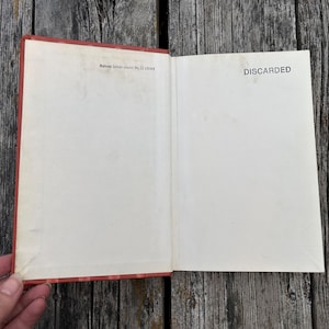 May include: An open hardcover book with a red spine and cover edges. The inside front cover and endpaper are off-white. The text "Wallowa School District No. 12 Library" is printed at the top left, and "DISCARDED" is printed on the right.