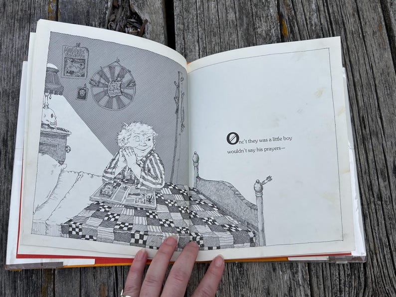 May include: An open illustrated book featuring a black and white line drawing of a child sitting in bed with a quilt. The text on the right page reads: "Onc't they was a little boy wouldn't say his prayers-". The illustration shows a bedroom scene.