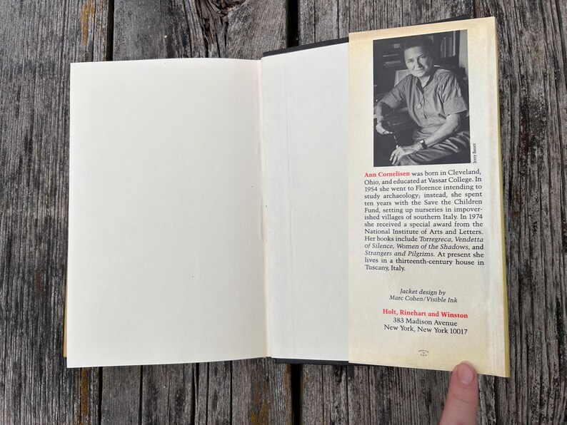 May include: An open hardcover book with a cream-colored page on the left and a dust jacket flap on the right. The flap features a black and white portrait of Ann Cornelisen above a biography and publisher information for Holt, Rinehart and Winston.