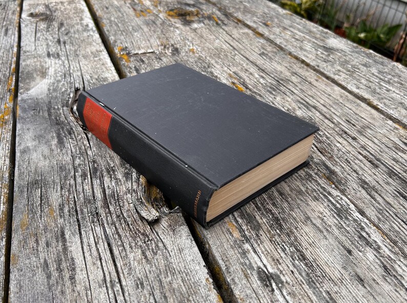 Pu&ograve; includere: Un libro con copertina rigida nera e un accento rosso sul dorso. Il libro presenta pagine di colore chiaro visibili lungo il bordo. Il dorso mostra un piccolo testo di colore dorato stampato verticalmente vicino alla parte inferiore.